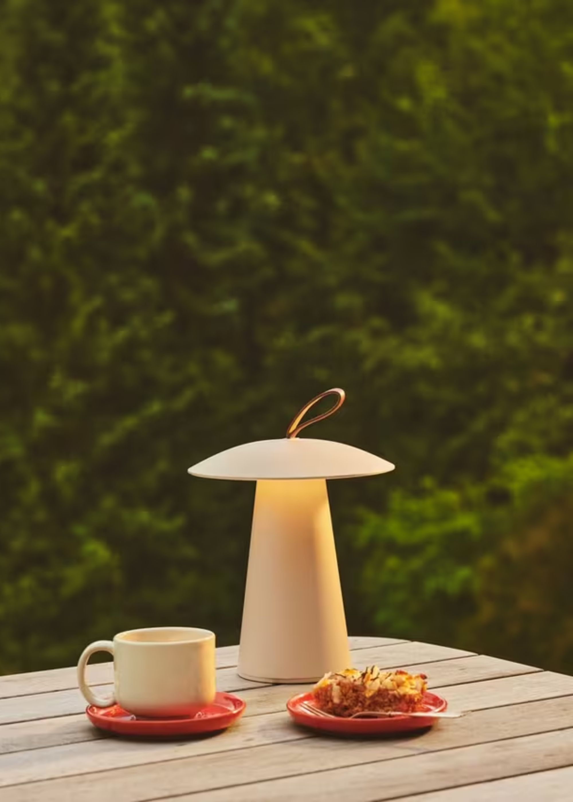 A portable lamp on an outdoor table with a mug and a baked good 