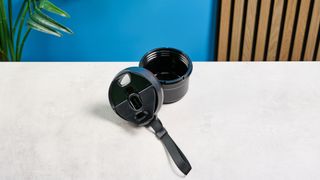 the Nutribullet Flip with a black insulated tumbler and a portable battery-powered blade photographed with a blue background. The tumbler has a carry strap and a sippy lid you can interchange, and an on/off button on the base.