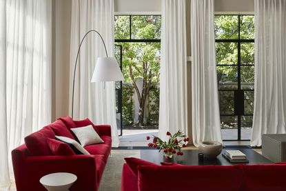 A living room with red sofas and long, white puddling curtains