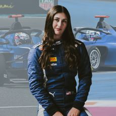 Lia Block from F1 Academy standing in front of two photos of blue race cars.