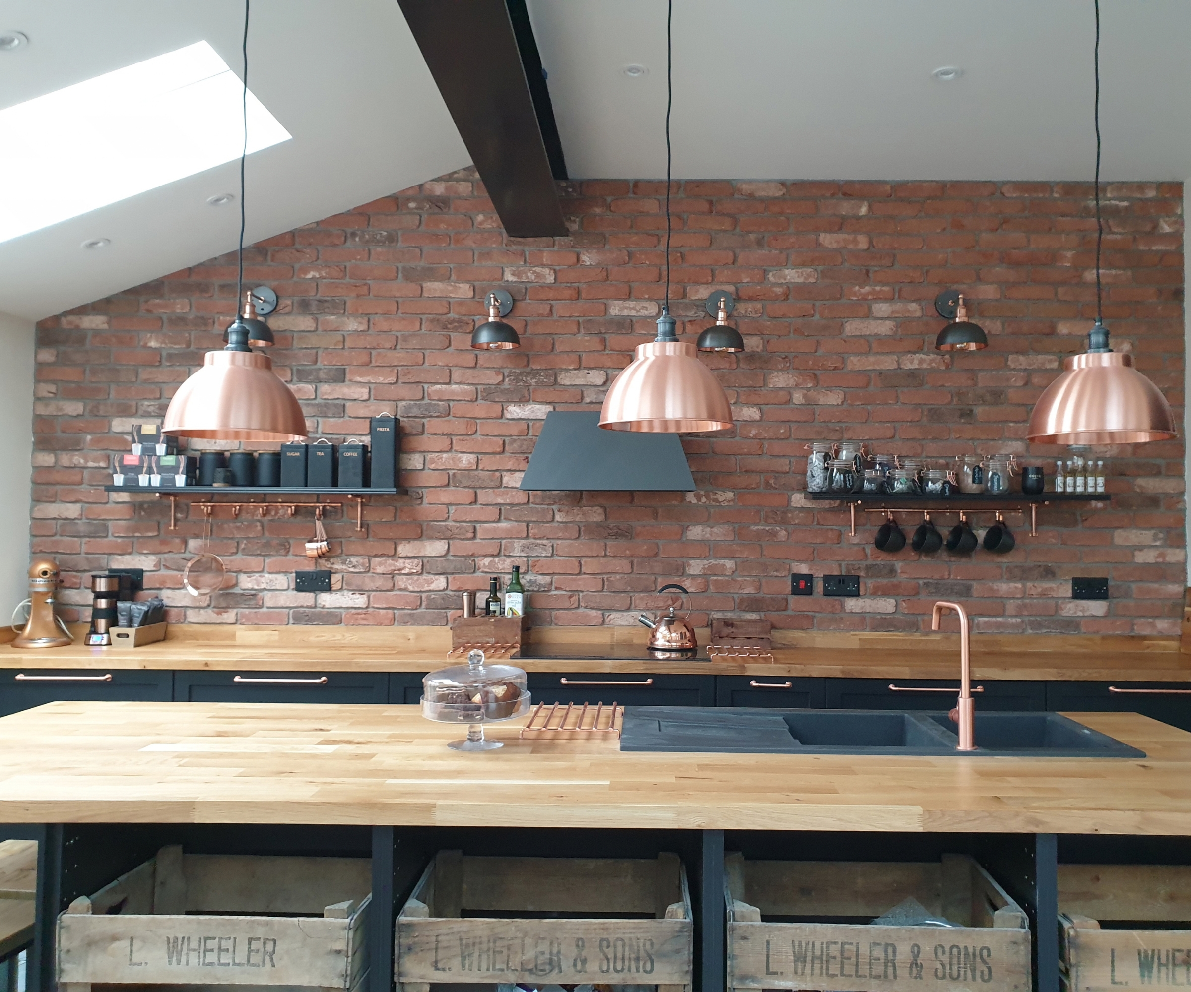 Industrial kitchen with exposed brick, copper pendant lights, black cabinetry, and vintage crates below the island.