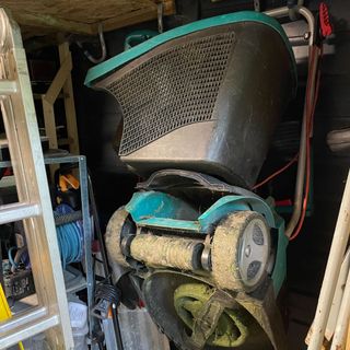 Green and black lawn mower hanging on the wall in a shed