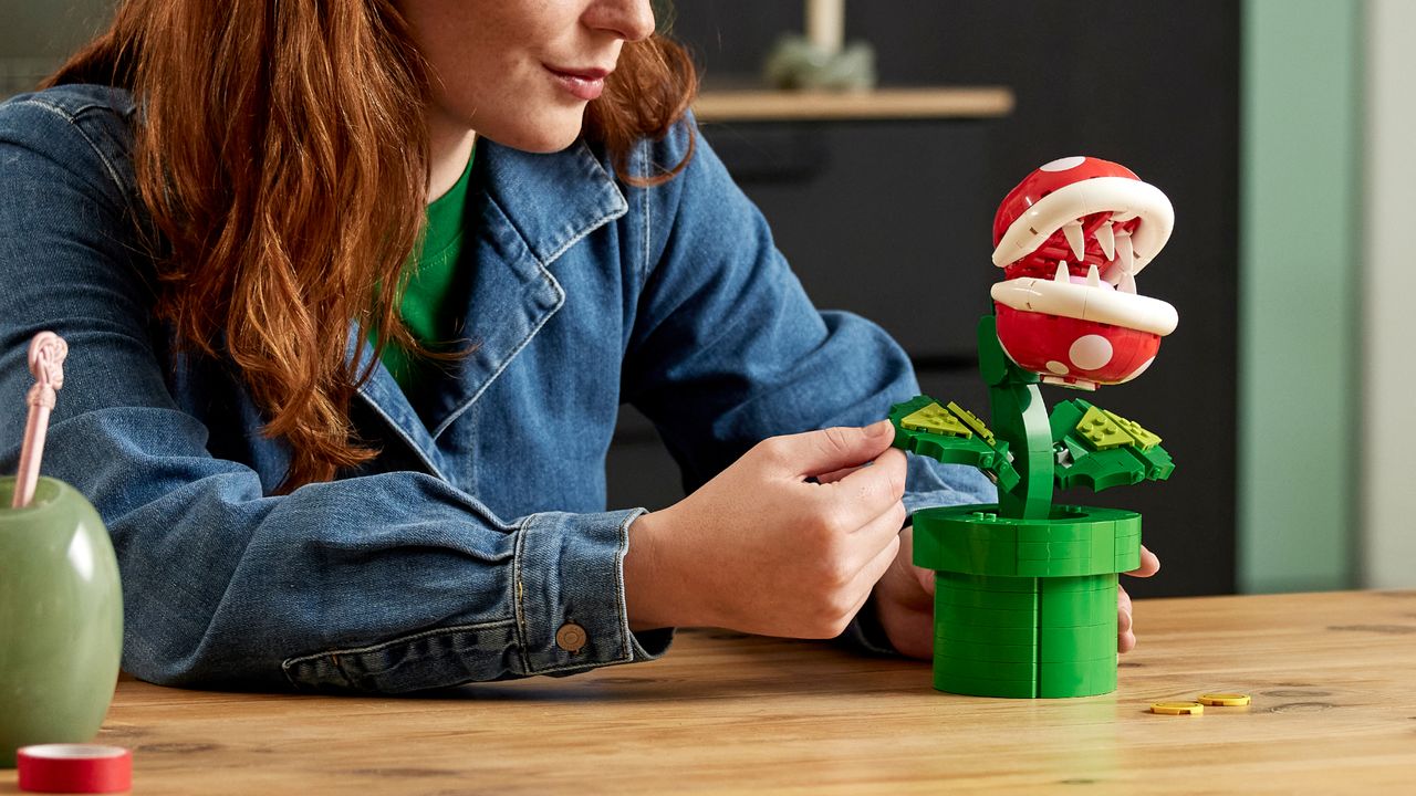 A woman at a table moves the leaf of the Lego Piranha Plant