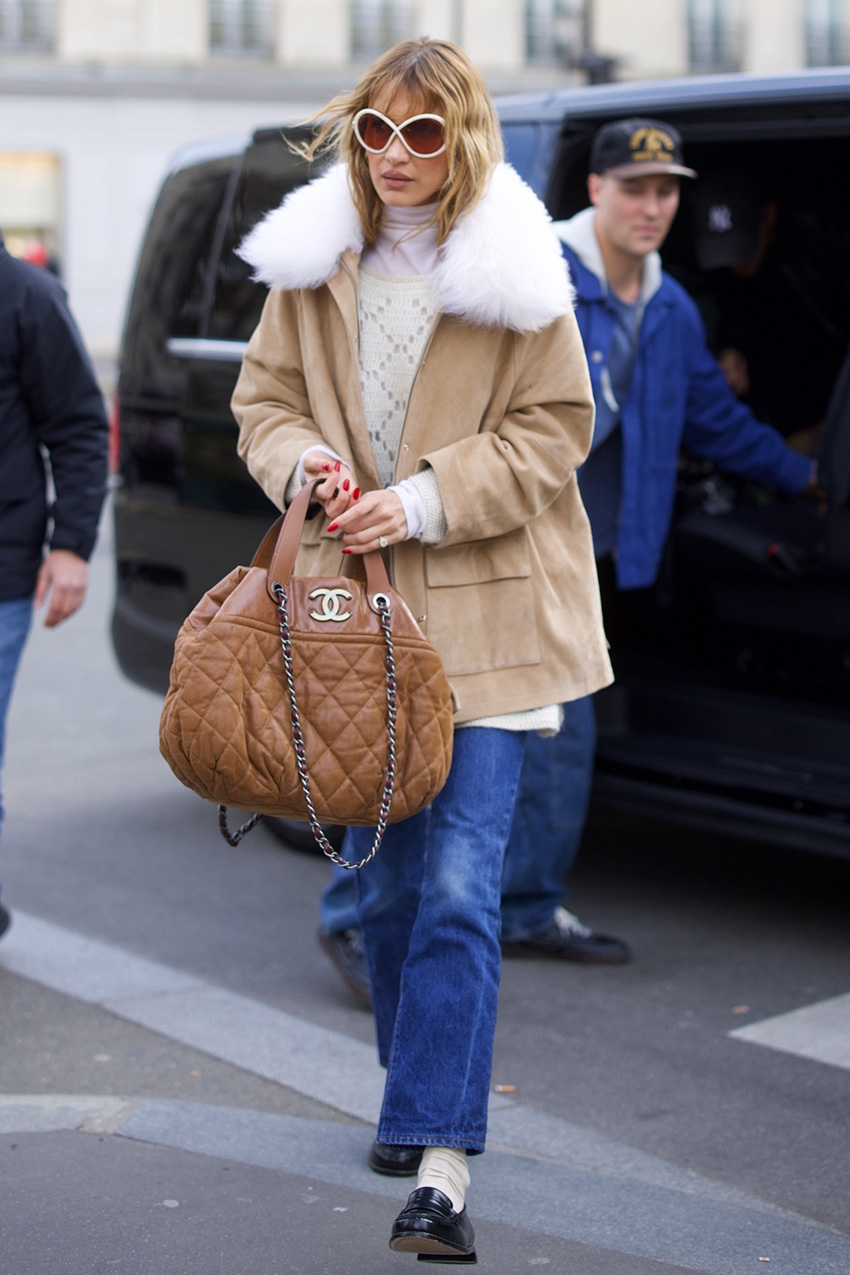 Bella Hadid wearing a tan coat, cream sweater, cropped flare jeans, socks, and loafers in Paris during PFW F/W 26