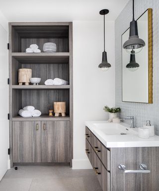 Grey open cupboard shelving with hanging pendant lights over white ceramic sink