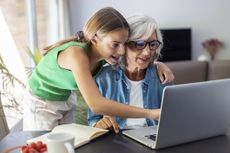 Shot of happy granmother using laptop with her granddaughter at home.
