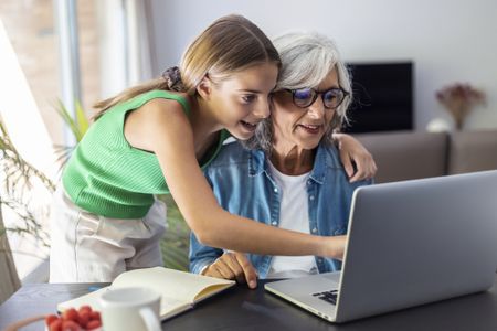 Shot of happy granmother using laptop with her granddaughter at home.