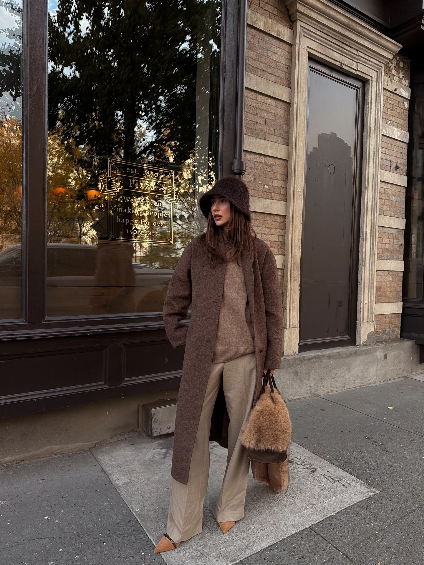 A woman wears a faux fur scarf with a coat and pants.