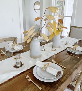 Rustic Friendsgiving table setup with foliage in vases and cloth runner