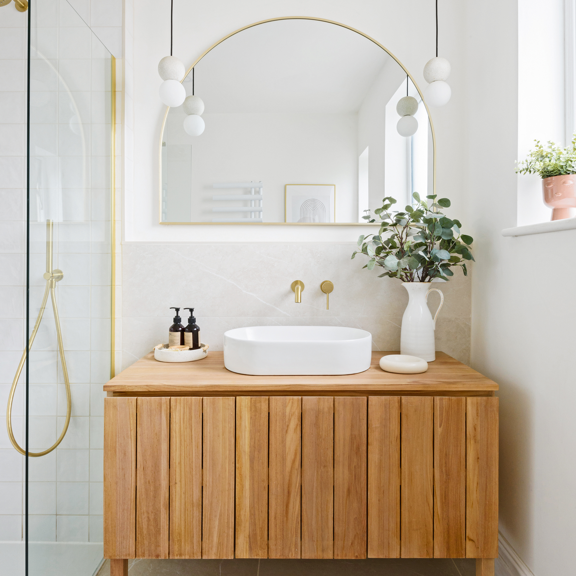 a shower enclosure with glass panels, beside a wooden vanity unit and half-moon wall mirror
