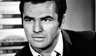 Dan August Burt Reynolds sitting in his office, with an open collar