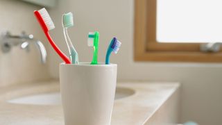 Toothbrushes sitting in a cup on the side of a bathroom sink together
