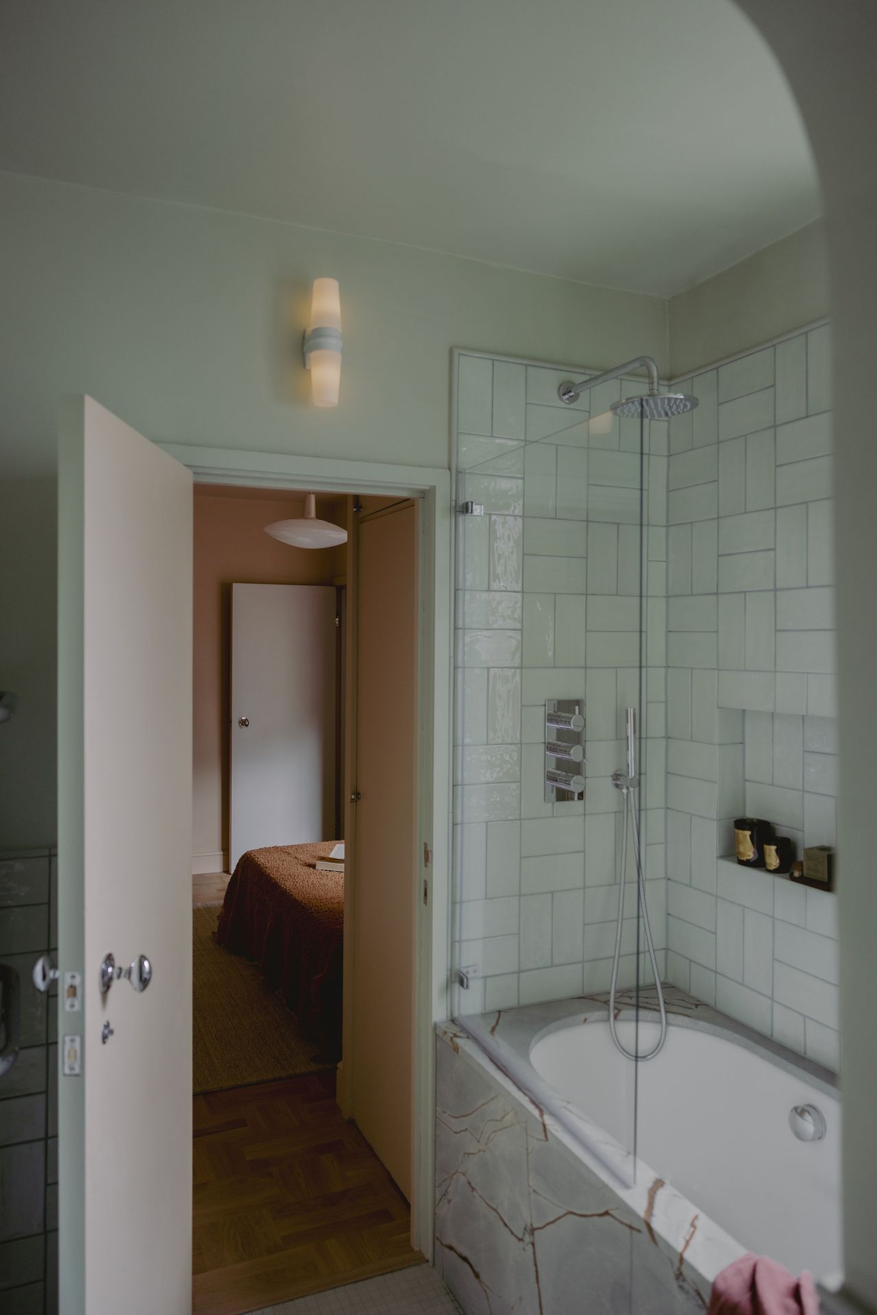 Image of a cyan/light teal bathroom with a marble bathtub. The door is open to a peach bedroom.