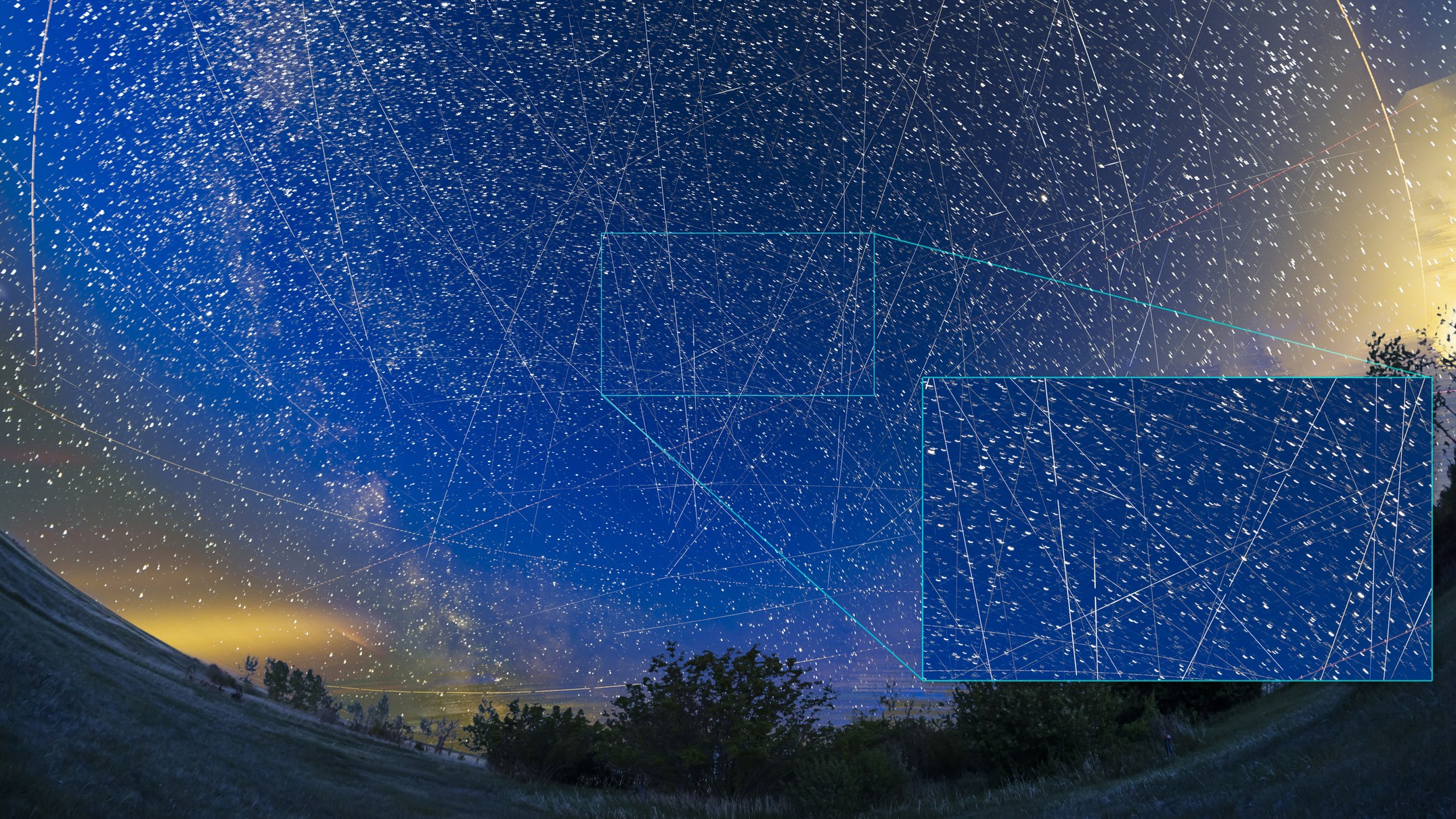 view of night sky filled with stars and long white streaks of light coming from the satellites.