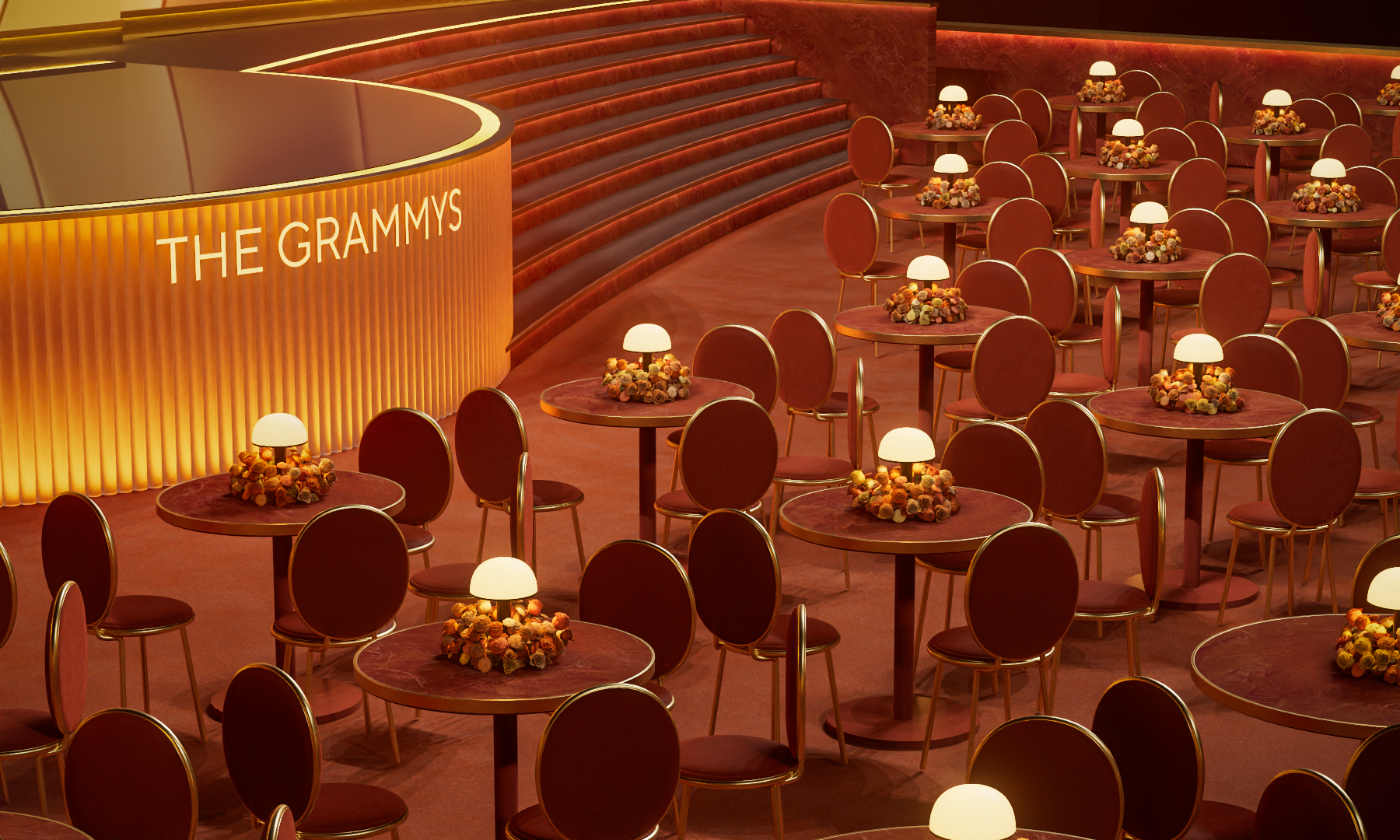 An aerial view of a performance stage with a sculptural, abstract structure of orange, red, and yellow swathes, foregrounded by a series of ceremony round tables with lamps as centerpieces.