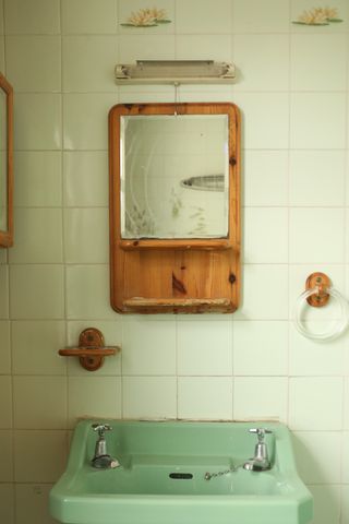 A dated bathroom with a wooden mirror, an avocado sink, and discolored wall tiles