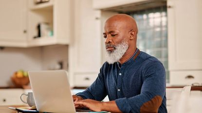 A mature man using a laptop at the kitchen table