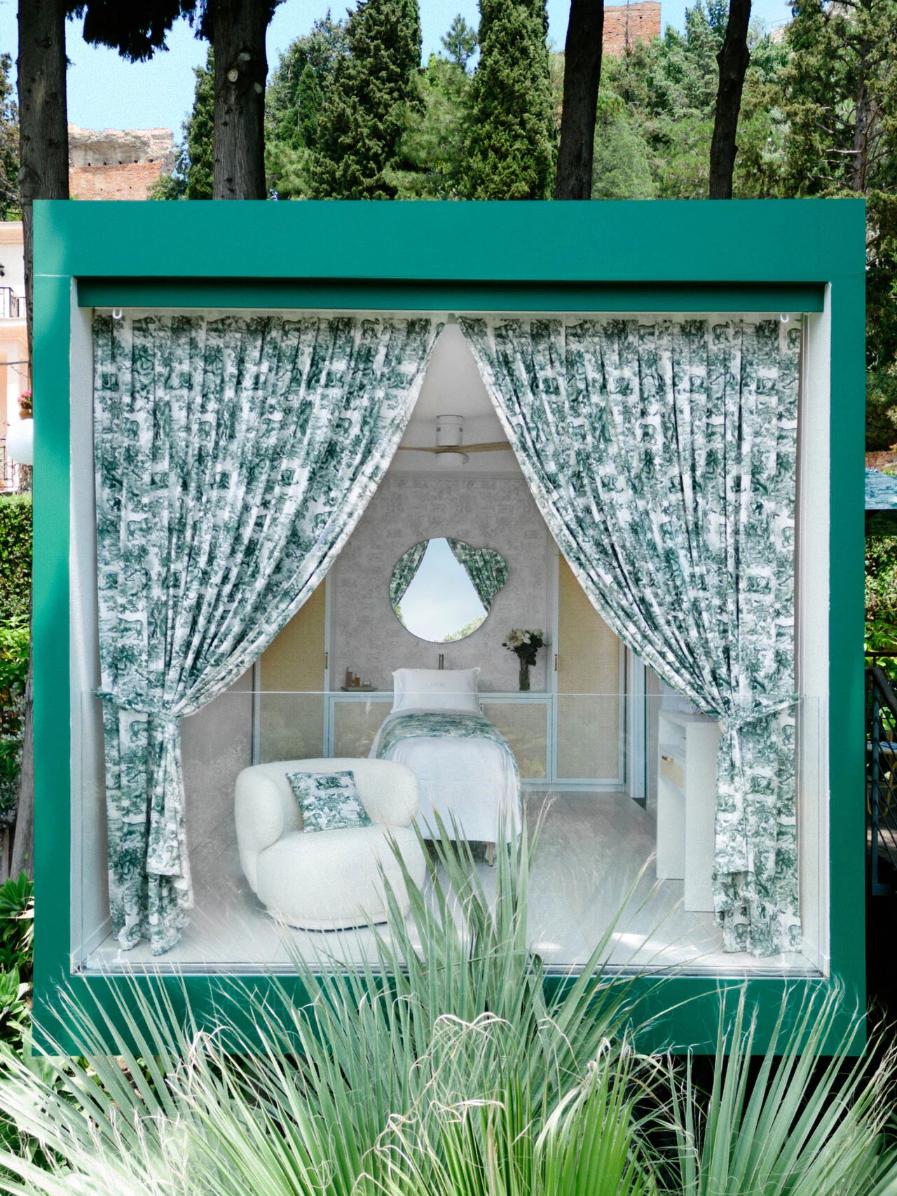 A Dior-branded medical spa sits atop a lush hilltop in Sicily in a green-tinted, square bungalow structure immersed in Mediterranean nature.