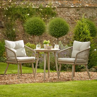 woven outdoor furniture bistro set in a garden with a stone wall