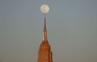 A 99 percent illuminated Pink Moon rises behind the Empire State Building as the sun sets in New York City as seen from Hoboken, New Jersey on April 15, 2022.