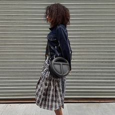 A wearing a denin jacket, plaid skirt, and silver shoes with a black Telfar bag 