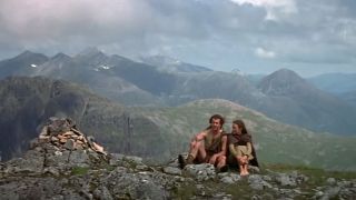 Two people sitting on a mountain top with a magnificent vista behind them in Braveheart