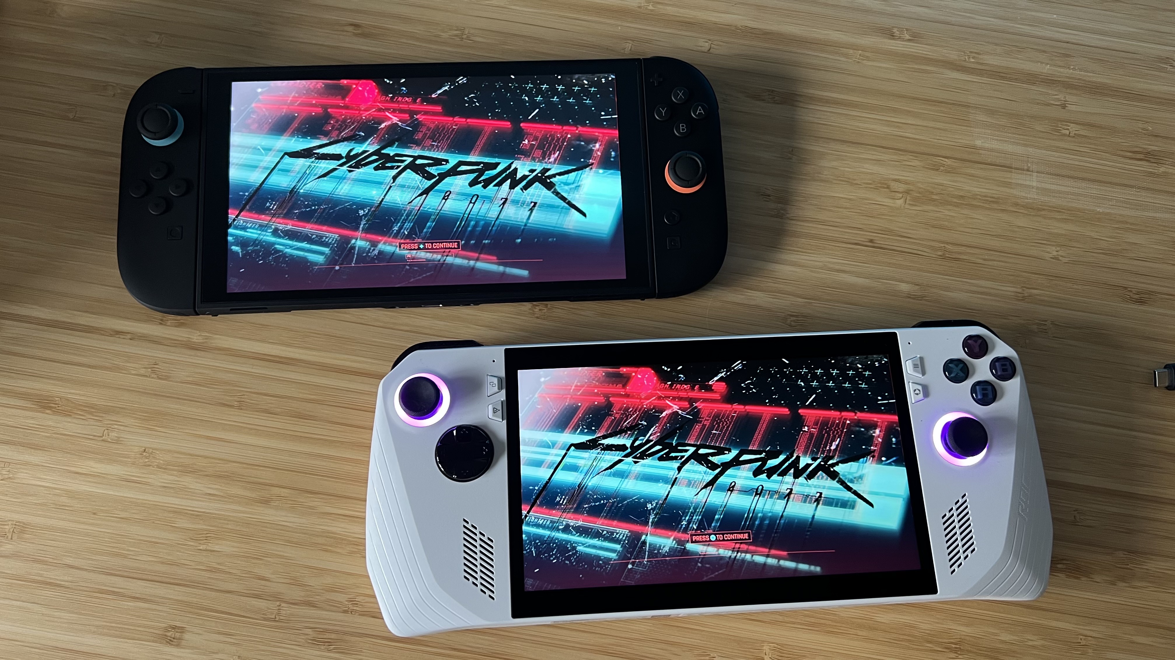 Nintendo Switch 2 and Asus ROG Ally running Cyberpunk 2077 on a wooden desk