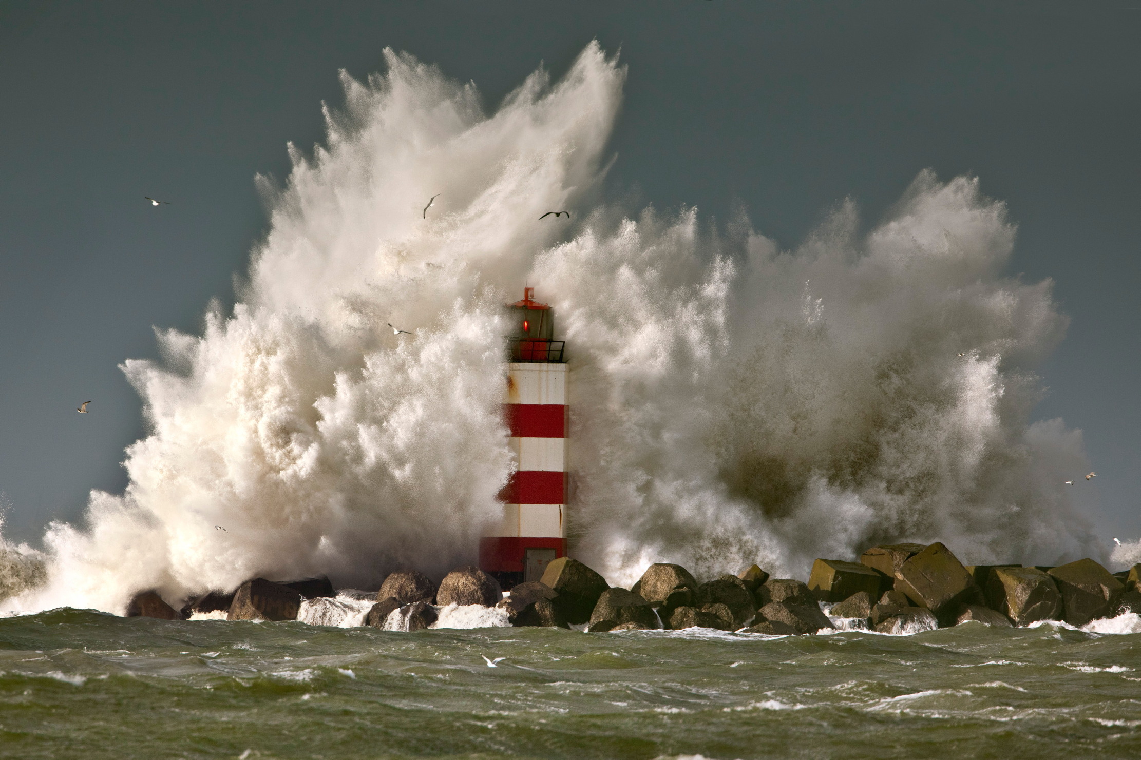 A wave crashes over a lighthouse. it looks jolly windy