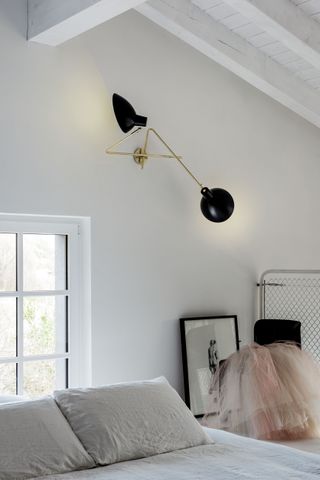 A white bedroom with black and brass wall light, framed art and pink tulle material