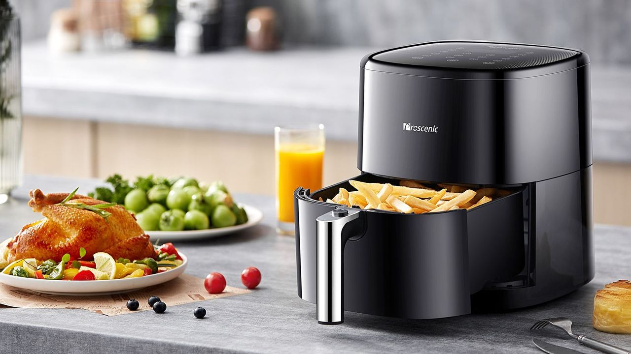 Proscenic T22 Air Fryer on a kitchen counter, filled with fries, beside a plate of roast chicken.