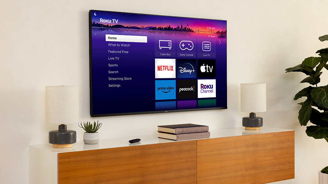 Roku Pro Series TV wall mounted above a wooden media unit with lamps, plants and books on