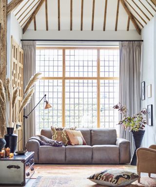 A modern rustic living room with grey low-seated sofa, wooden beams, vintage trunk and vases