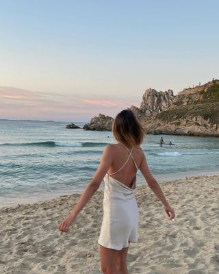 Woman standing on beach with back to camera wearing a slip dress.