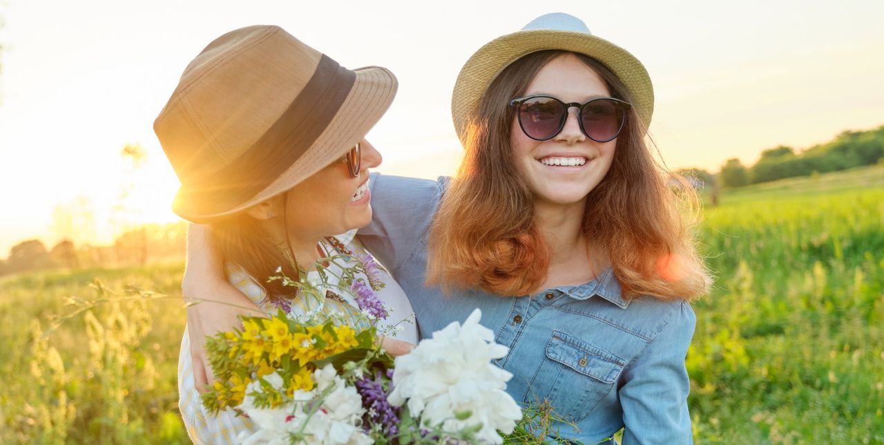 Mothers day, hugging happy smiling daughter with mother in meadow with bouquet of spring flowers