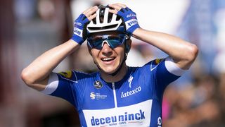 Remco Evenepoel of Belgium in cycling helmet and sunglasses holds his hands up in celebration