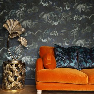 Dark palm print wallpaper behind orange sofa and metallic palm light