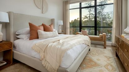 A bedroom with a calming neutral palette, a large window, and a cream throw on the bed