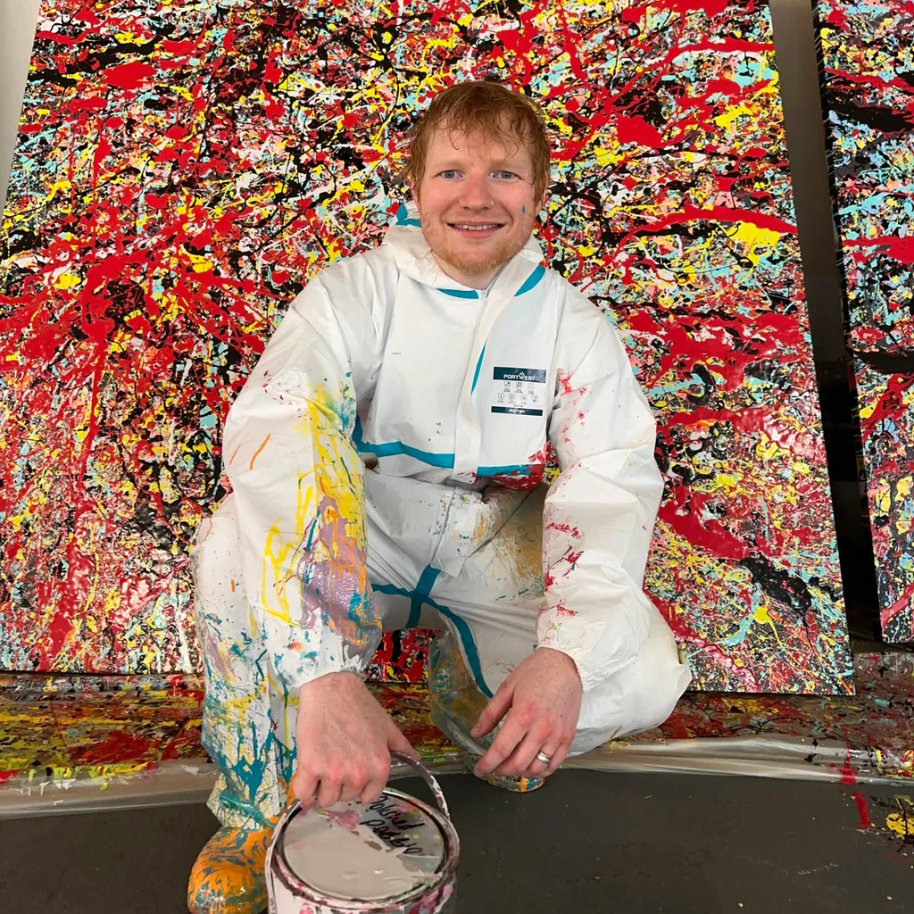 Ed Sheeran crouching in front of a Pollock-esque painting