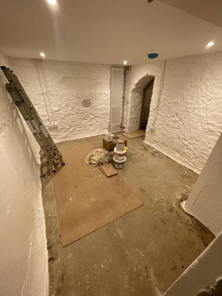 The lounge area underground in the air raid shelter before the renovation with painted white brick walls and flagstone tiled floor
