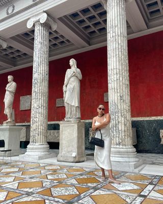 Jasmine Fox-Suliaman wearing a white slip dress, mesh ballet flats, and a black shoulder bag at an art museum in Copenhagen.