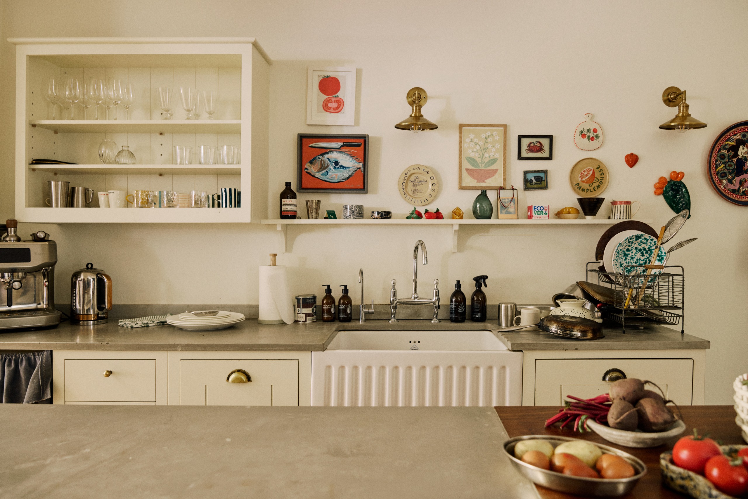 Image of white kitchen with lots of decor on the walls and open shelving filled with a mix of glassware, cookware, and kitchen utensils.