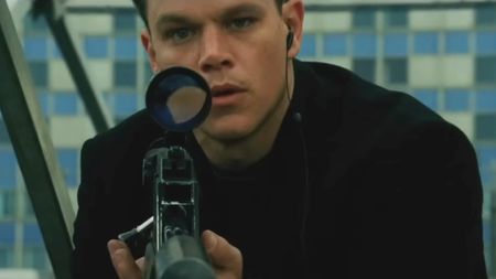 Matt Damon holds a sniper rifle while looking surprised in The Bourne Supremacy.