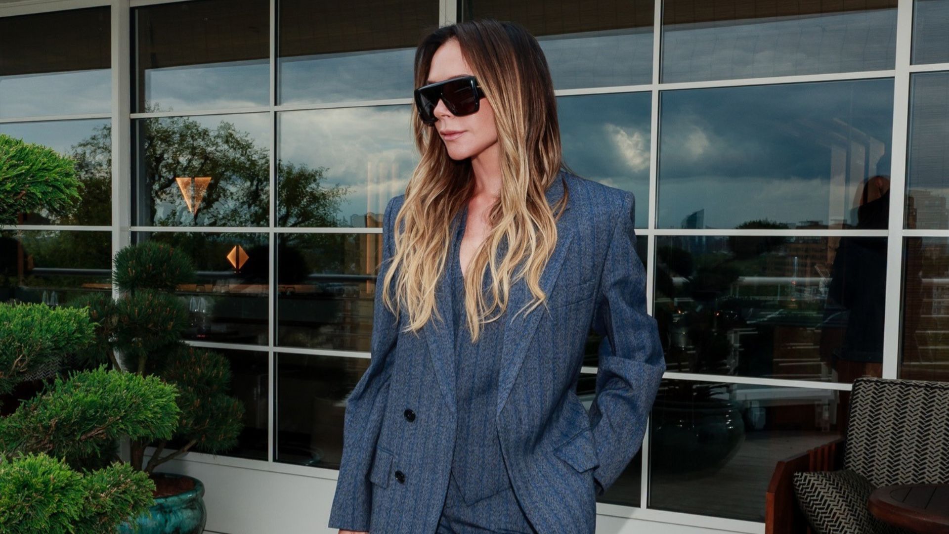 Victoria Beckham wears a striped suit with patent leather croc print heels and oversized sunglasses.