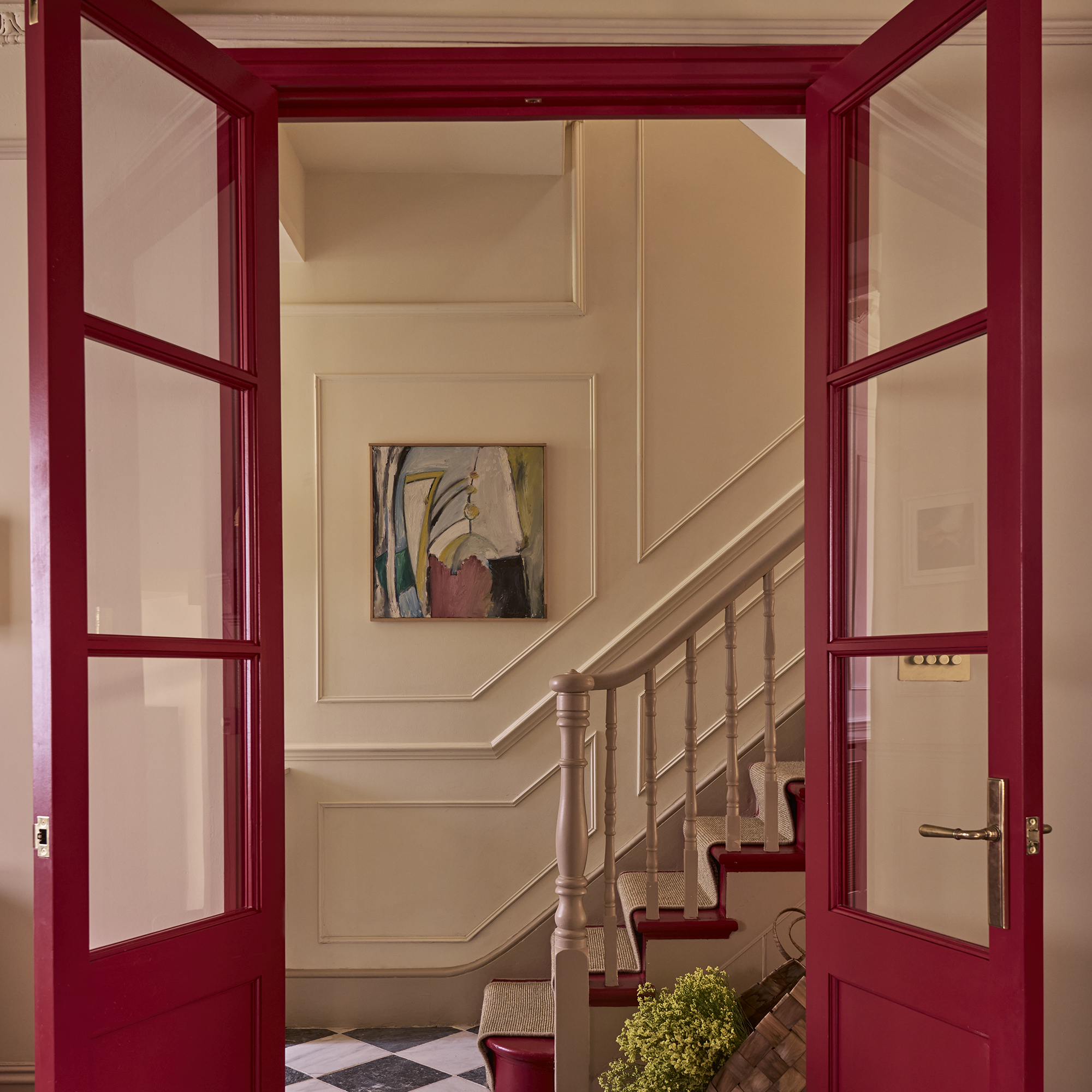 red internal glazed double doors opening onto a pale pink hallway with a staircase with the stairs painted in the same red shade
