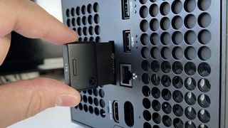 A person inserting a small black Seagate Storage Expansion Card into an Xbox Series X console.
