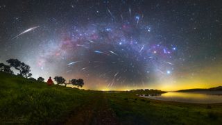 streaks of bright light crisscross the night sky above a tree-lined lake