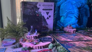 The Horizon Forbidden West: Seeds of Rebellion box, board, miniatures, and tokens on a table filled with wood and fake plants