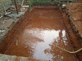 A soakaway hole being dug in a garden with water being sprayed into it