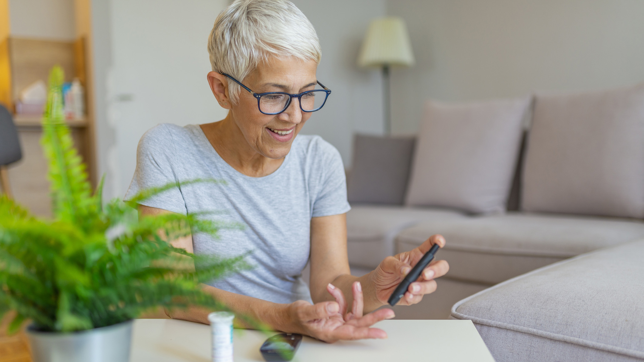 A woman with short white hair uses a glucometer to measure her blood sugar levels at home