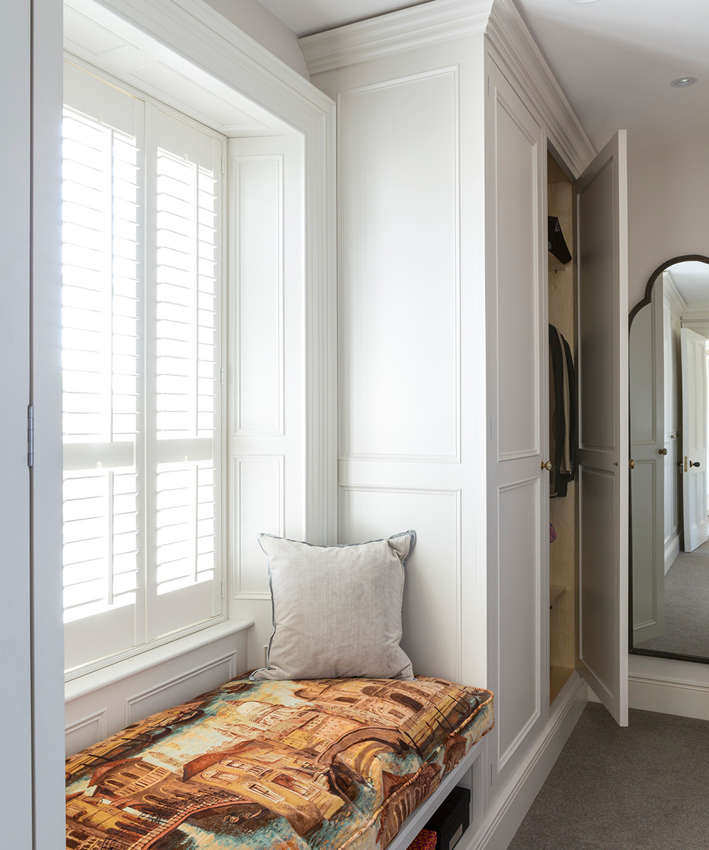 A window seat in front of a window with shutters